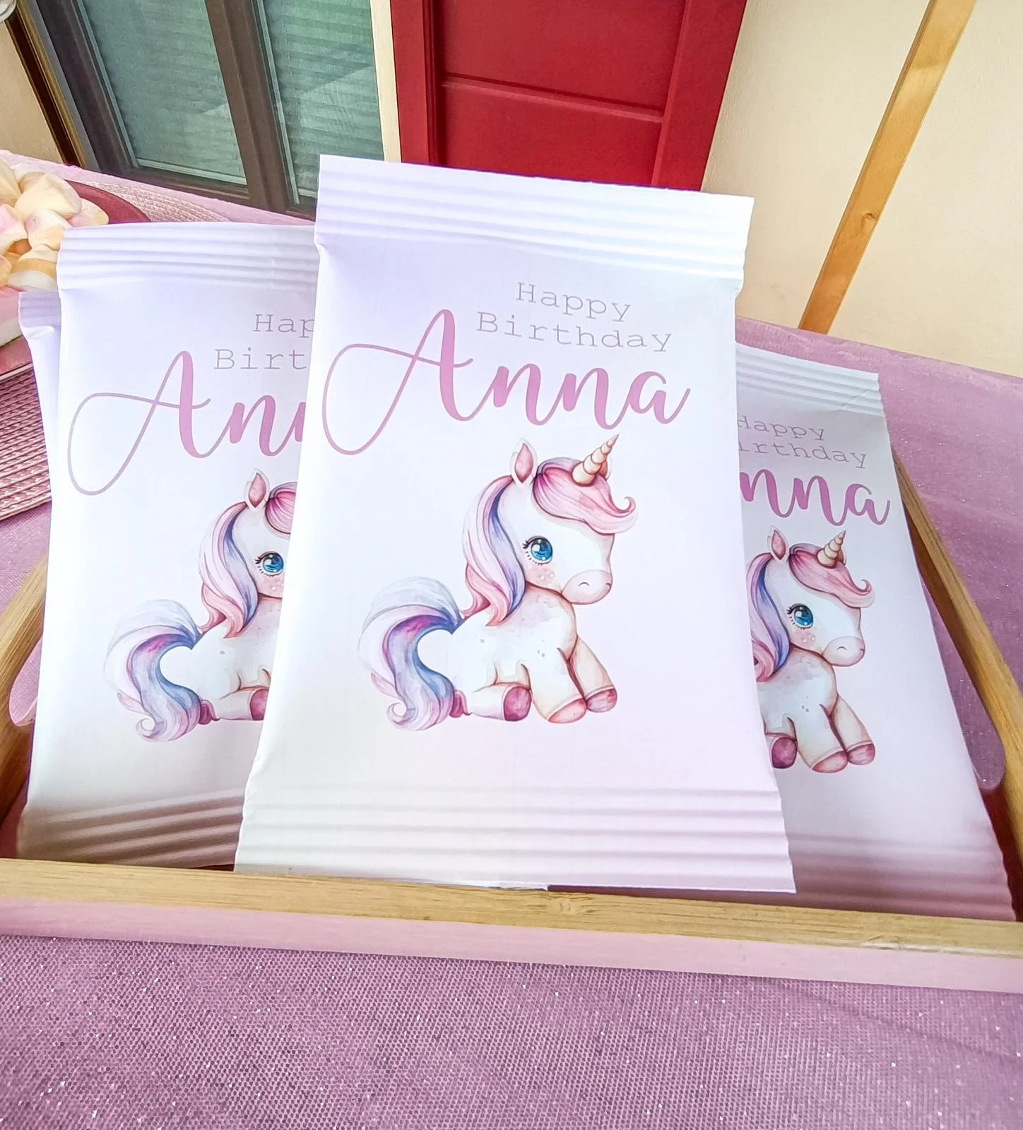 Biglietti di auguri con un unicorno rosa e azzurro e la scritta "Happy Birthday Anna" su una superficie rosa
