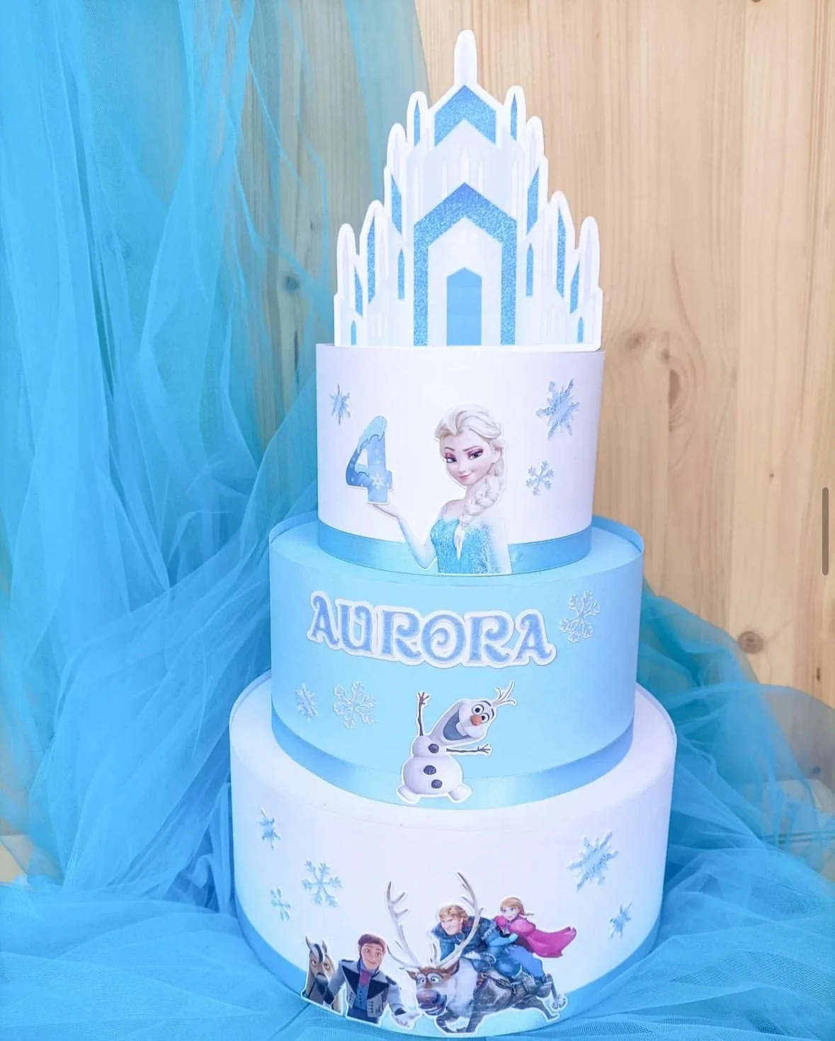Torta a tre piani con temi di Frozen e Olaf, decorazioni di neve e un castello di ghiaccio sulla cima, con personaggi di Frozen, Olaf e Sven, e il nome Aurora.