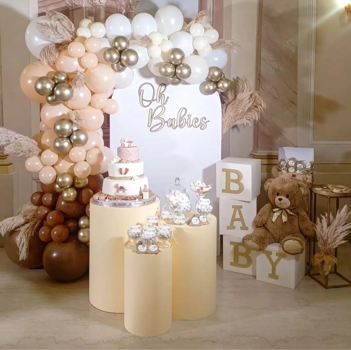Decorazioni per una festa di neonato con palloncini color pastello, un dolce, scritto 'Oh Babies', cubi con le lettere B, A, B, Y e un orsacchiotto di peluche.