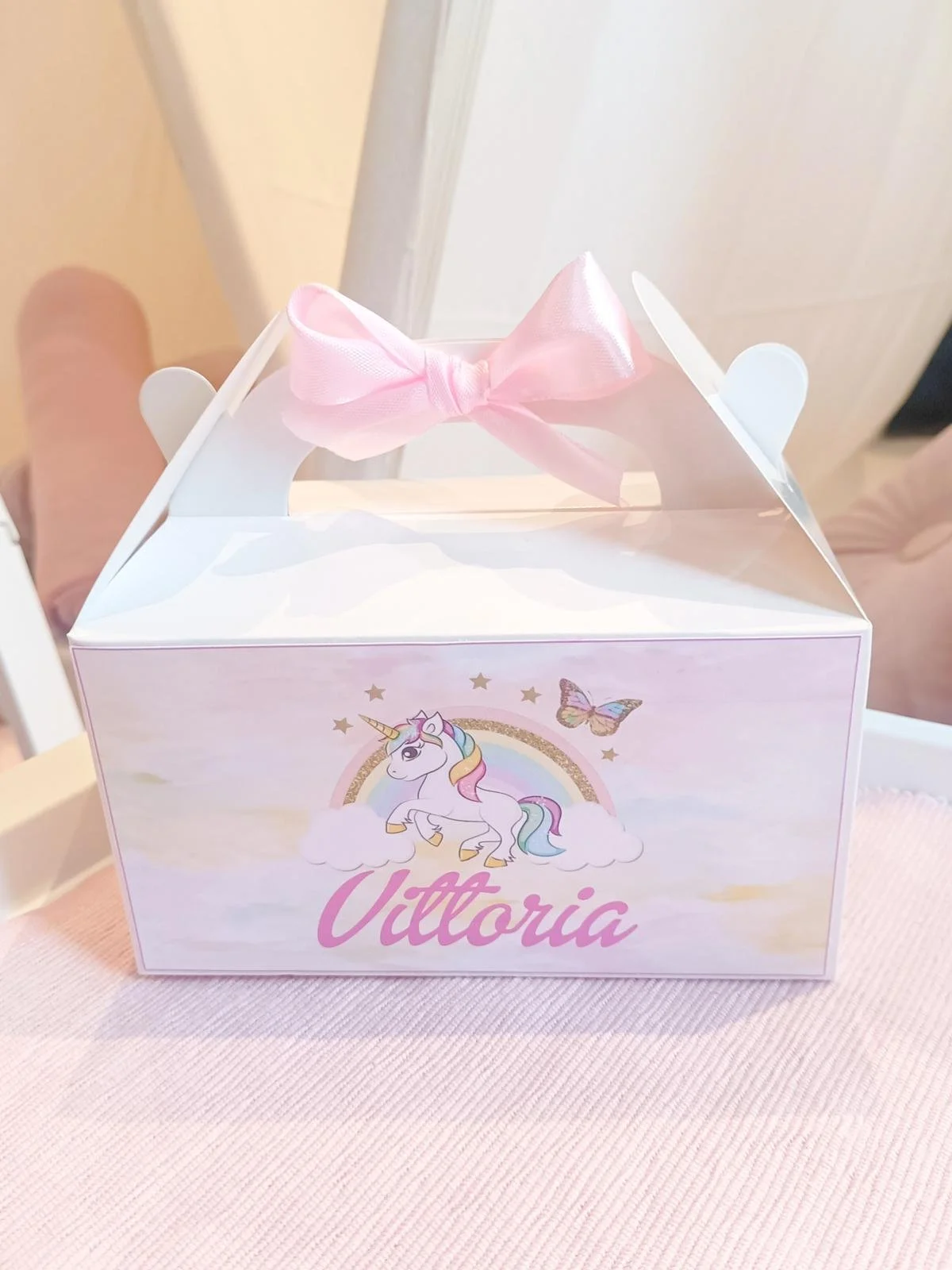 Scatola regalo bianca con decorazioni di unicorno, arcobaleno e farfalla, con il nome 'Vittoria' scritto in rosa, decorata con un nastro rosa