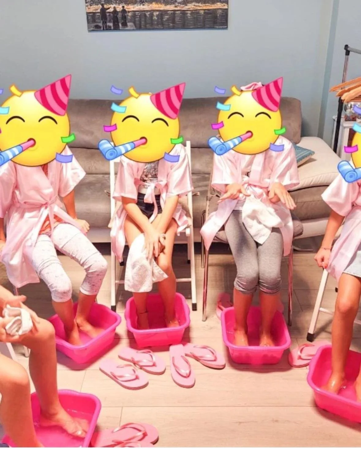Gruppo di persone con le facce coperta da emoji di faccina con cappellino, indossando accappatoi rosa e che stanno mettendo i piedi in secchi rosa, in un ambiente domestico.