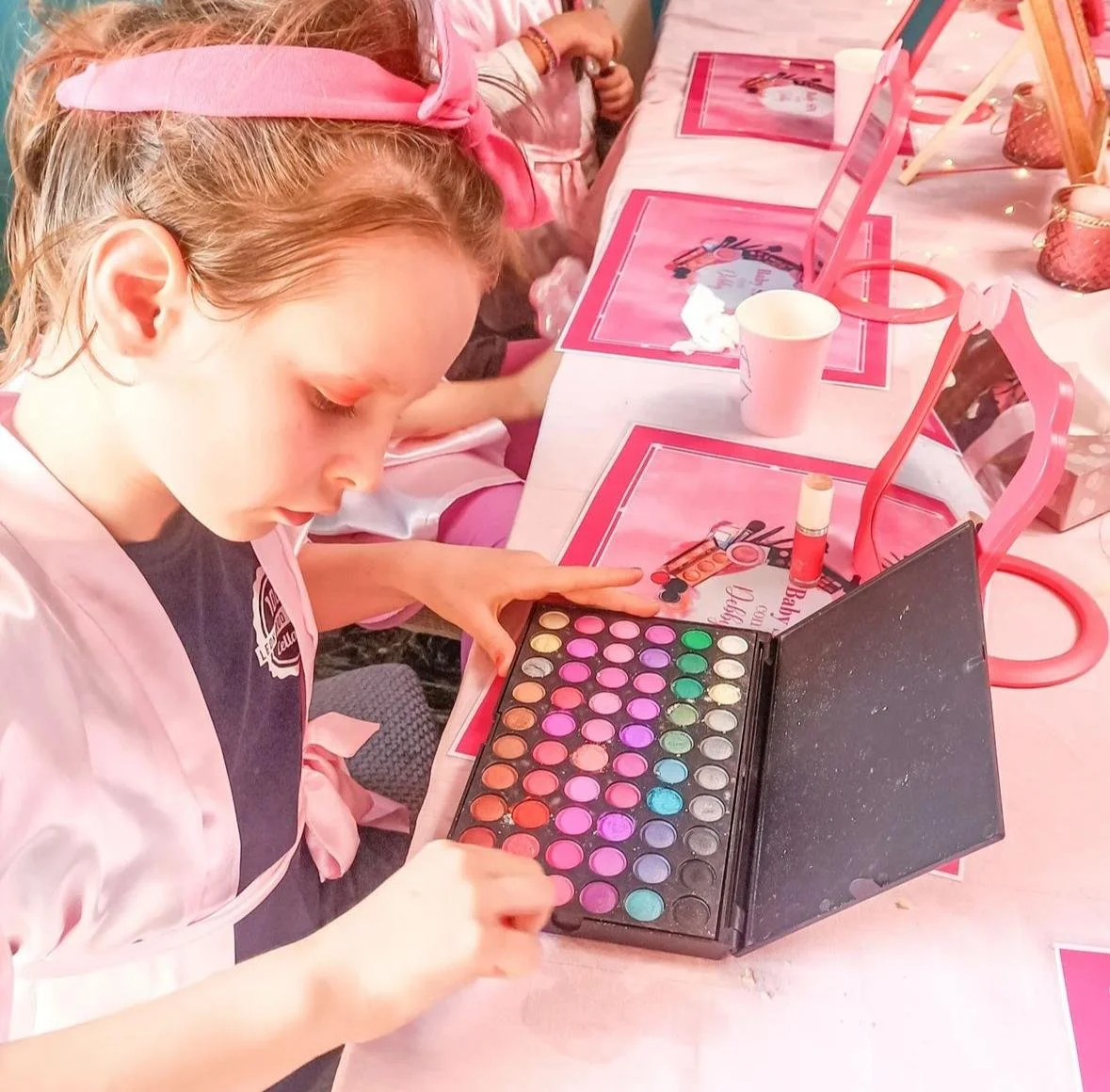 Ragazza che gioca con una palette di colori per truccarsi, con un'estetica rosa e rosa, in un ambiente decorato per una festa di Barbie.