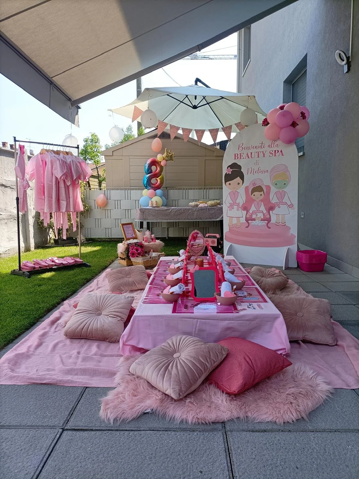 Decorazioni rosa e champagne per una festa al femminile con un cartellone che dice "Benvenuti alla Beauty Spa di Melissa" e un tavolo apparecchiato con piatti e copertine.