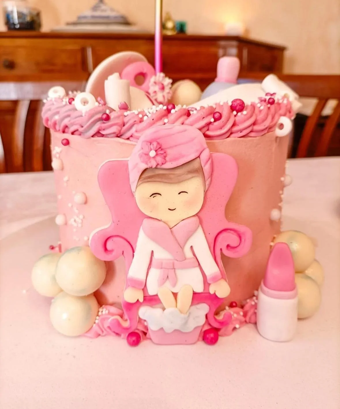 Torta di compleanno a tema bambina con decorazioni rosa, figura di una bambina sorridente in vestito rosa, e vari elementi decorativi come palline e rossetto.