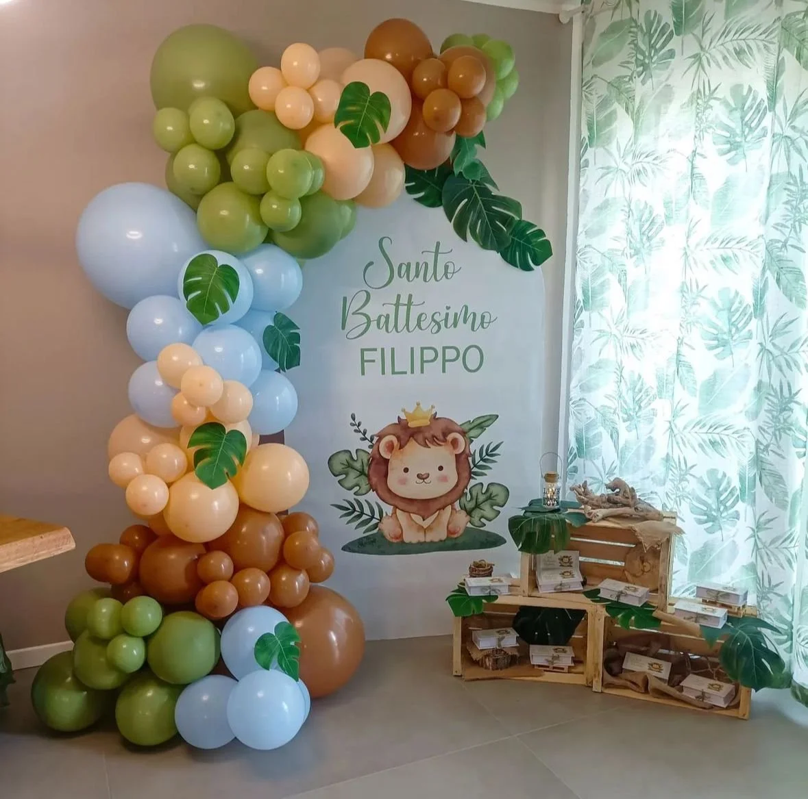 Decorazioni per il battesimo di Filippo, con palloncini colorati e foglie verdi, un pannello con un leone e il testo 'Santo Battesimo Filippo'.