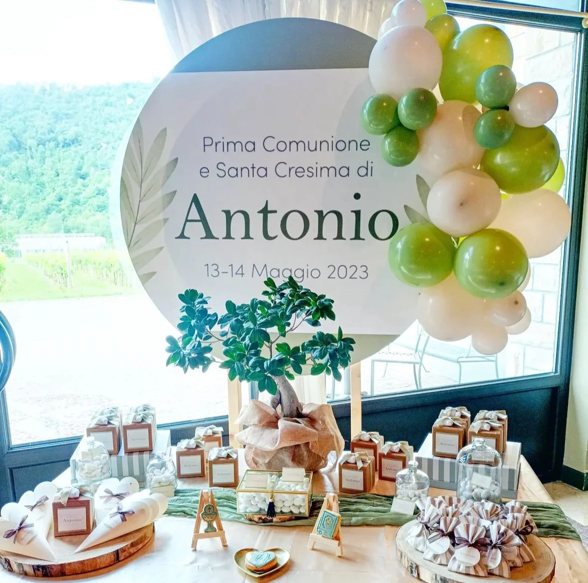 Decorazioni per la Prima Comunione e Santa Cresima di Antonio, con palloncini verdi, buste regalo, bomboniere e un albero decorativo, data 13-14 maggio 2023.