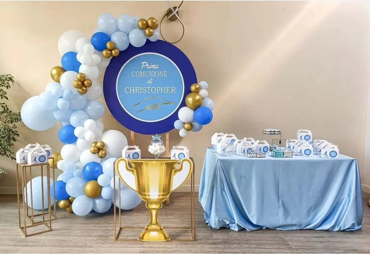 Decorazioni per la prima comunione di Christopher, con palloncini blu, bianco e dorati, una grande medaglia decorativa con il testo "Prima Comunione di Christopher", un tavolo con scatoline regalo e un grande trofeo dorato.