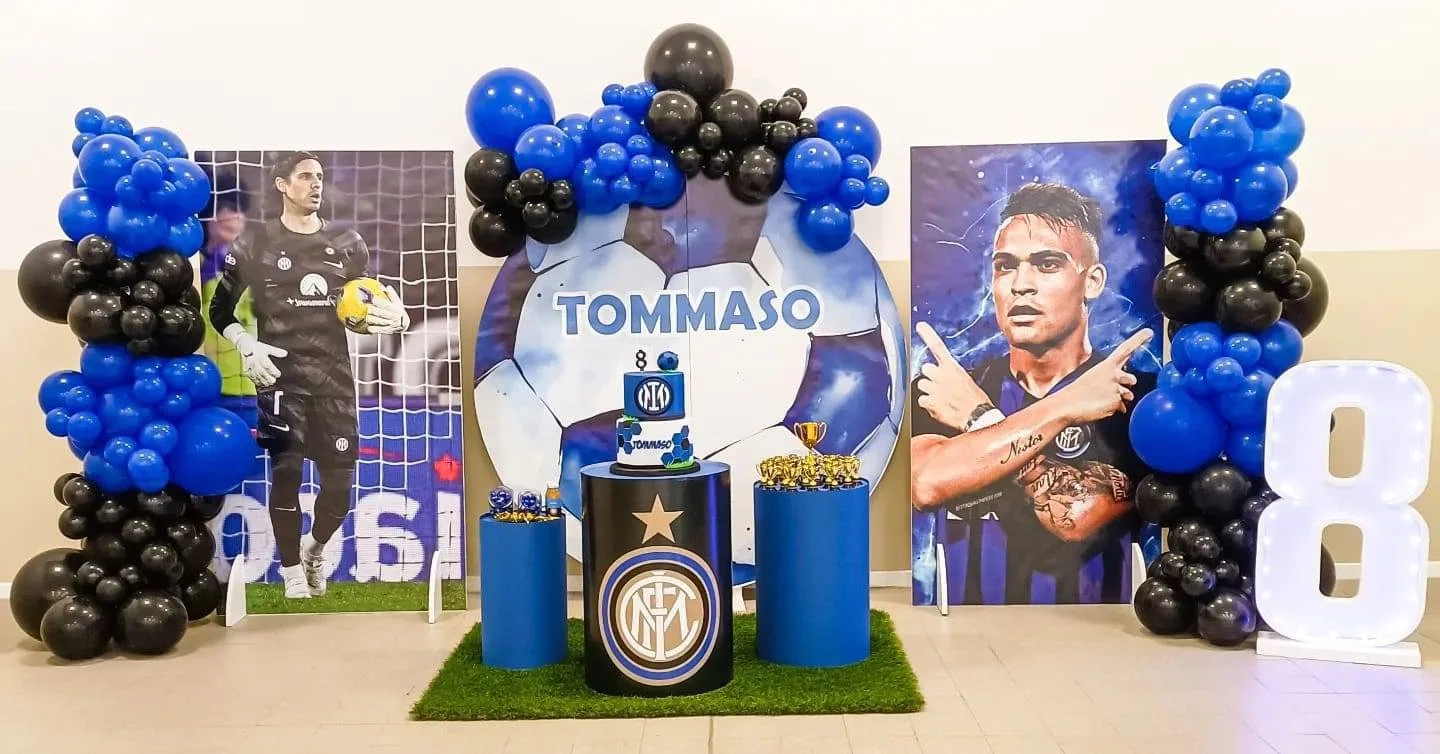 Decorazione per una festa di compleanno ispirata al calcio, con immagini di due calciatori, palloni, balloon blu e nero, un grande numero 8 e una torta con il nome Tommaso.