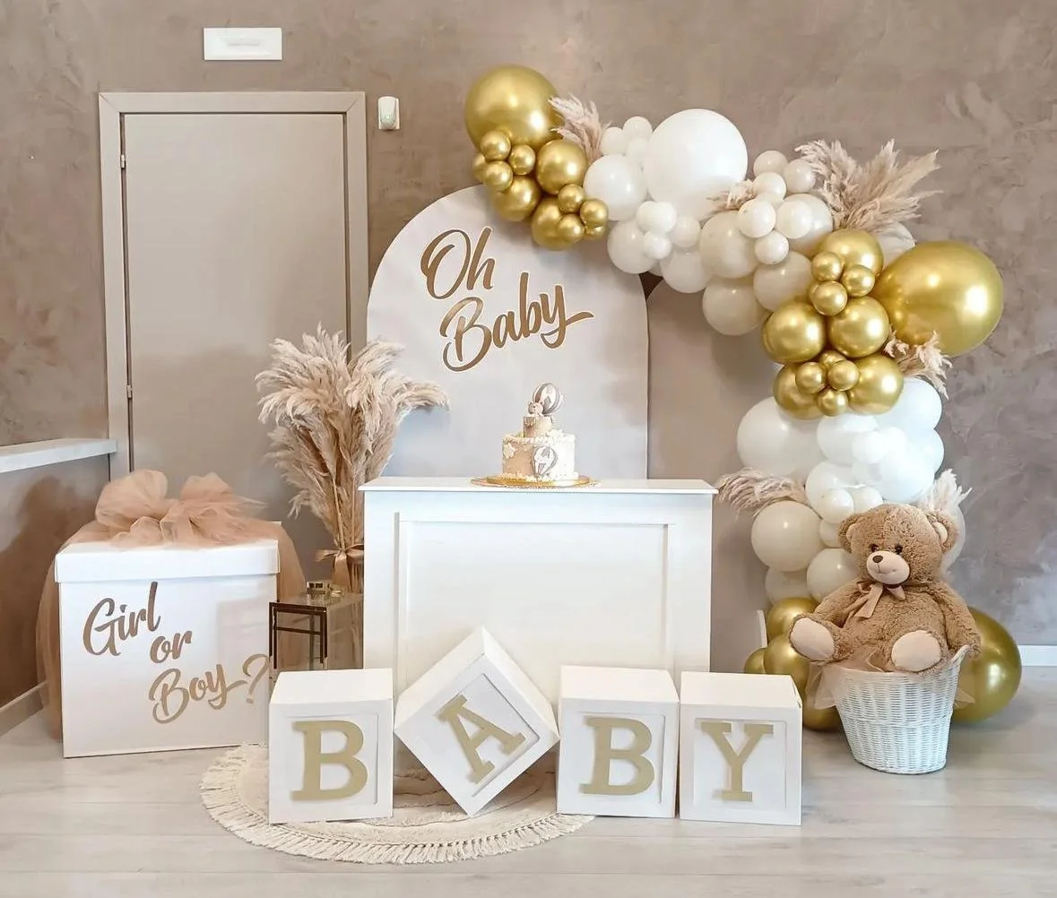 Decorazione per festa di benvenuto al bebè con palloncini bianchi e oro, Teddy bear in una cesta, e scatole con lettere che formano "BABY".