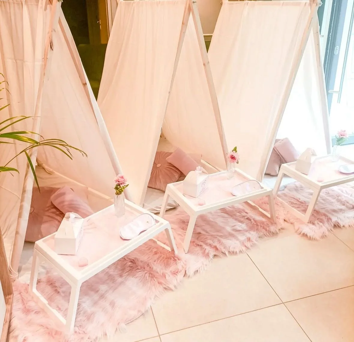 Tre aree di riposo con tende a baldacchino, cuscini rosa e tappeti pelosi rosa, con tavolini bianchi decorati con fiori e scatole di tovaglioli.