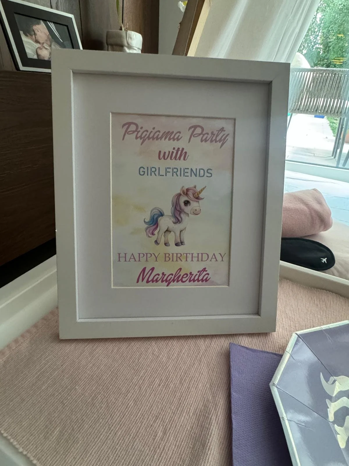 Cartello bianco con scritte rosa e blu e un disegno di un unicorno, che dice: "Pigiama Party with Girlfriends. Happy Birthday Margherita".